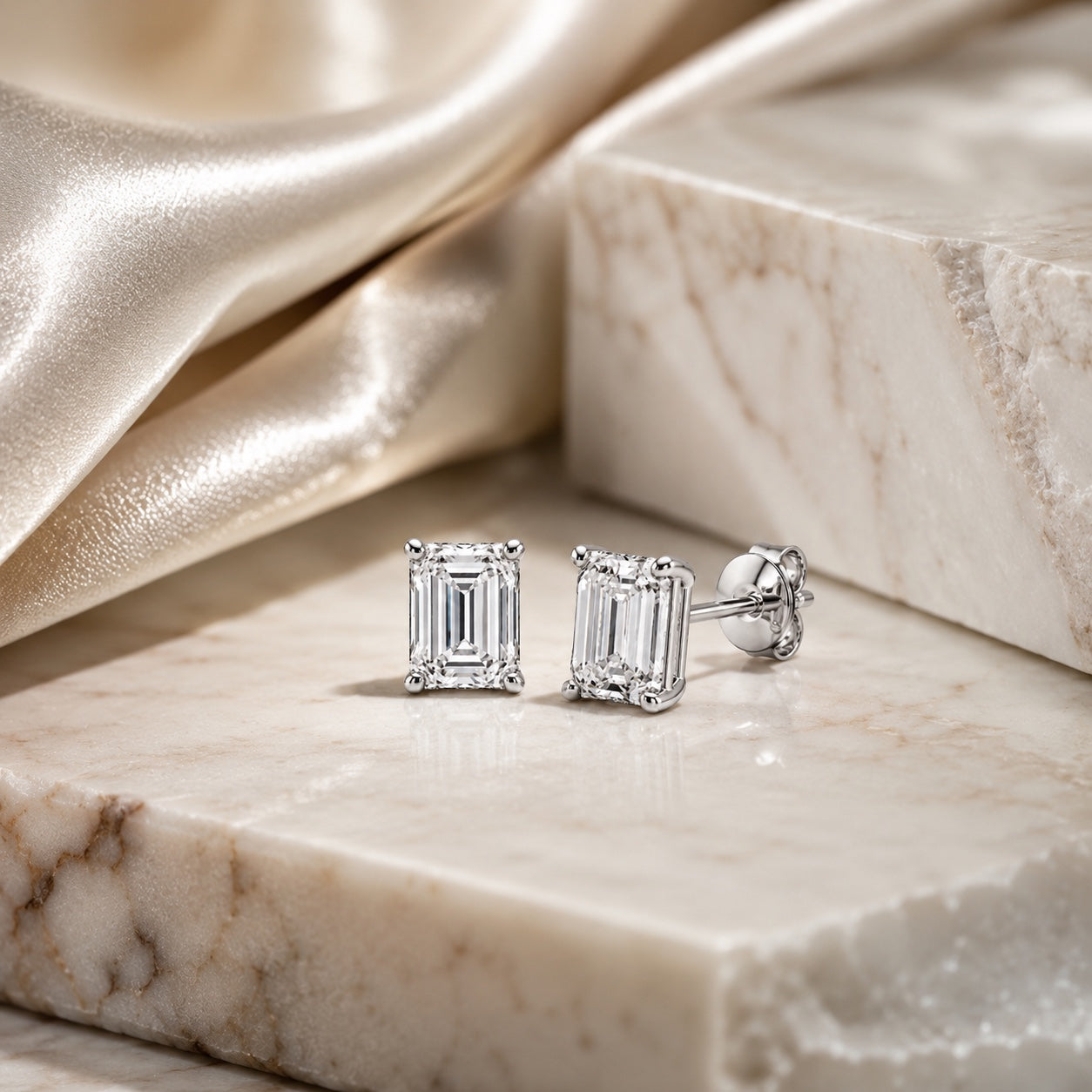 Editorial design render of emerald-cut 1.00 CTW lab-grown diamond studs in 14K white gold on marble and silk