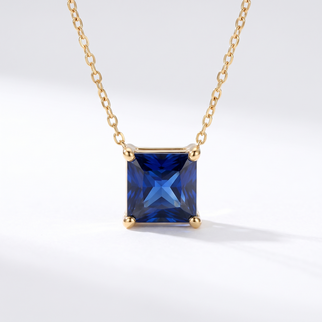 Princess-cut blue sapphire solitaire necklace in solid gold, catalog view — AI-generated design representation