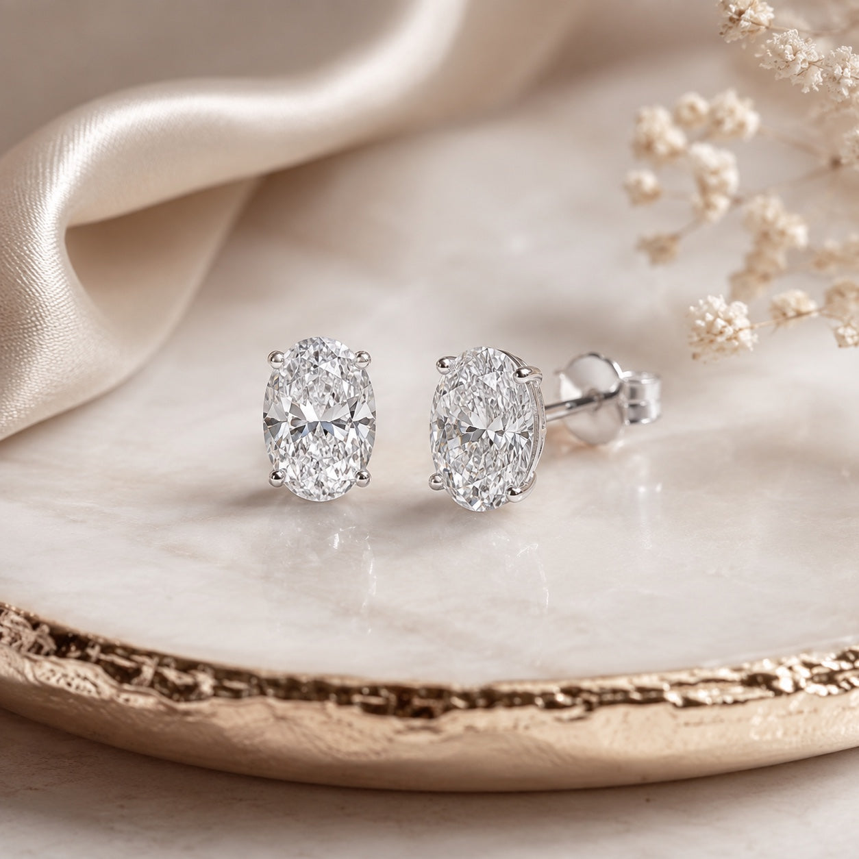 Editorial design render of oval 1.00 CTW lab-grown diamond studs in 14K white gold on marble and silk