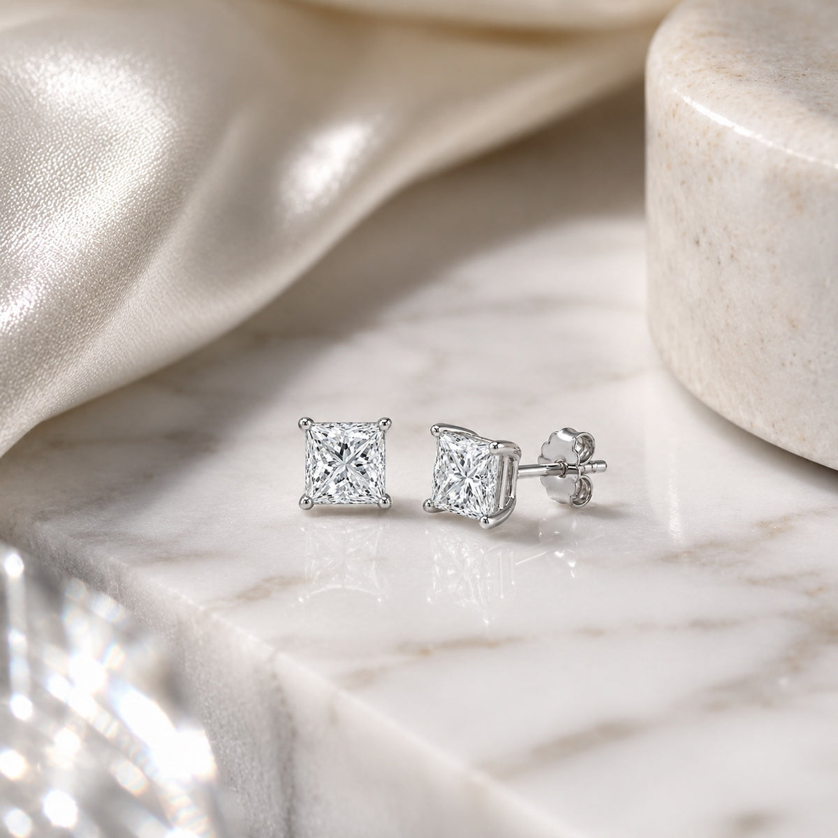Editorial design render of princess-cut 1.00 CTW lab-grown diamond studs in 14K white gold on marble and silk