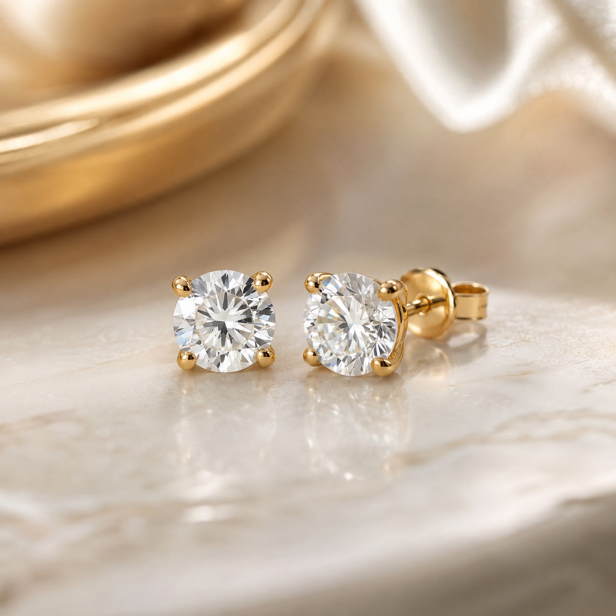 Editorial design render of round 1.50 CTW lab-grown diamond studs in 14K yellow gold on marble and silk